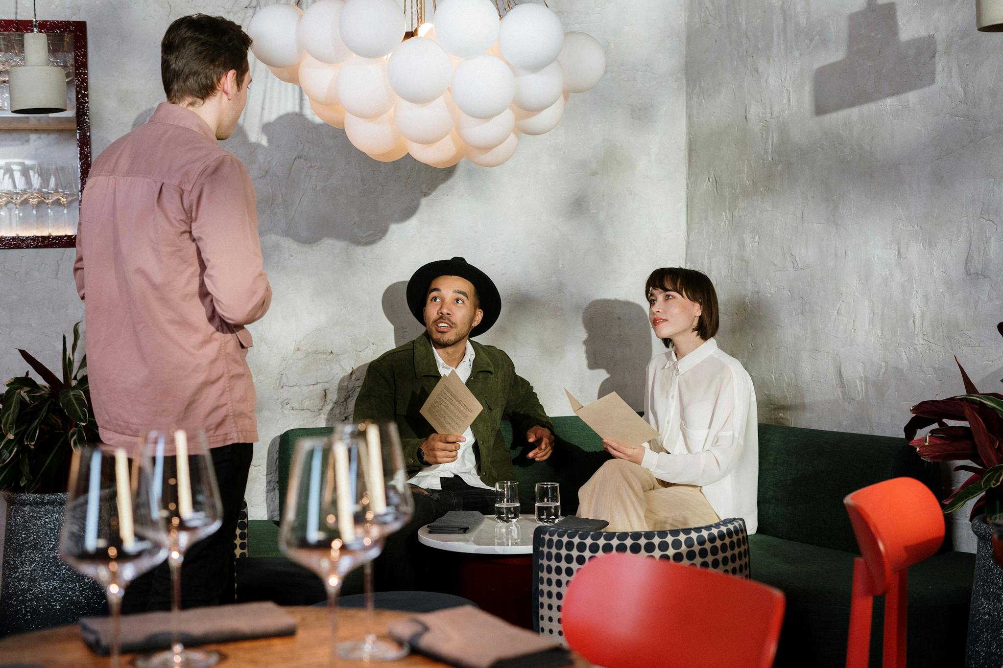 A couple reviews a menu at a chic restaurant, engaging with a waiter.